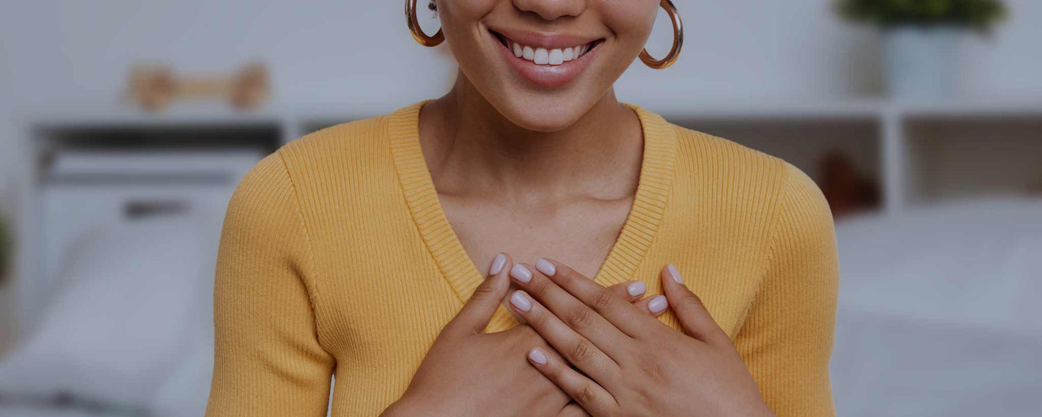 A smiling Black young lady holds her hands over her chest.