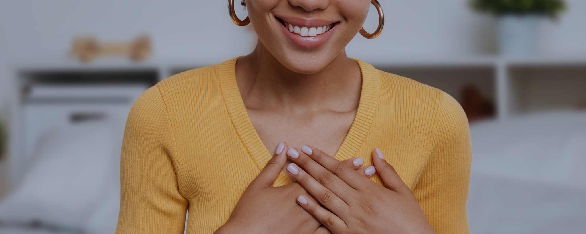 'A smiling Black young lady holds her hands over her chest.'