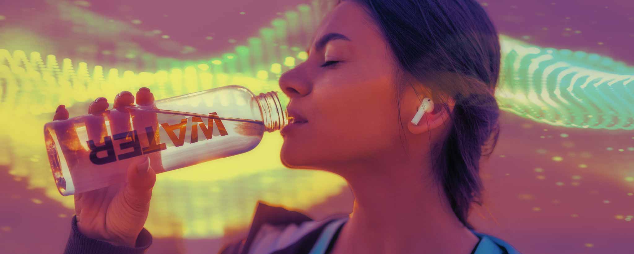 A female wearing earbuds drinks water.