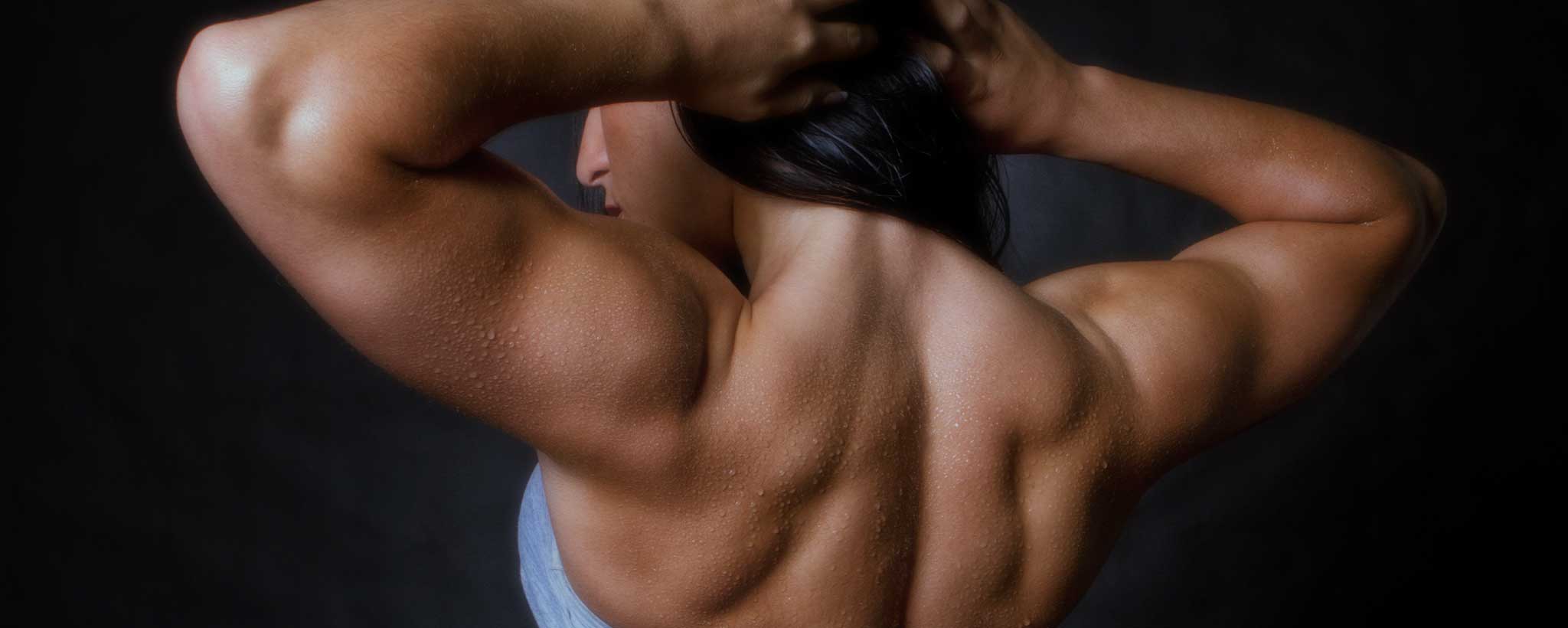 'A female bodybuilder flexes her back muscles.'