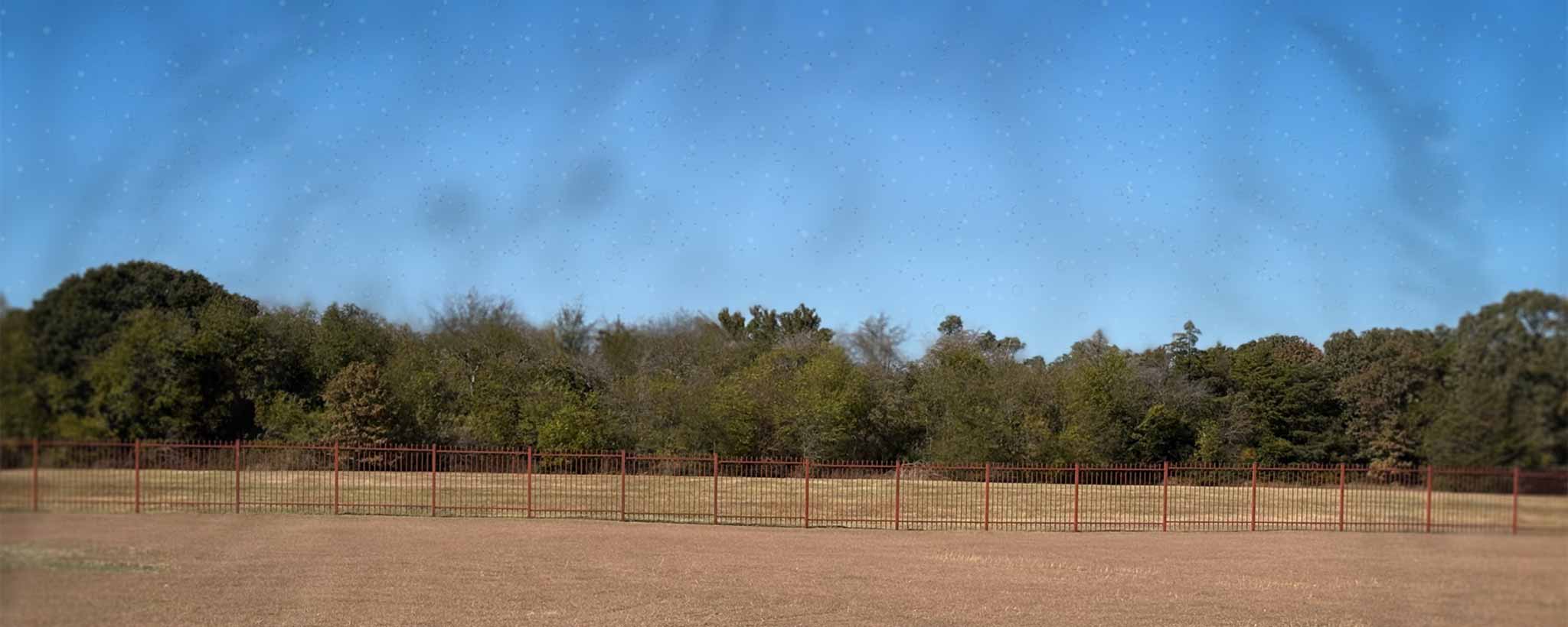'Open field with a fence and trees under a clear blue sky with floaters.'