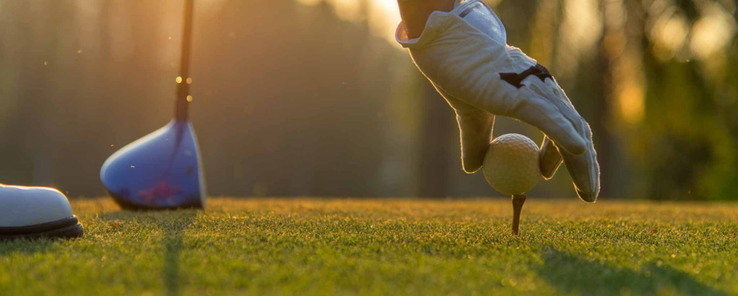 A golfer's hand places a ball on the tee.