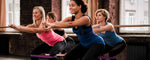 Four women in athletic wear perform a synchronized exercise in a studio.