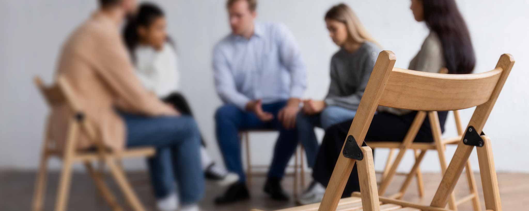 'A therapy support group sit in chairs facing each other.'