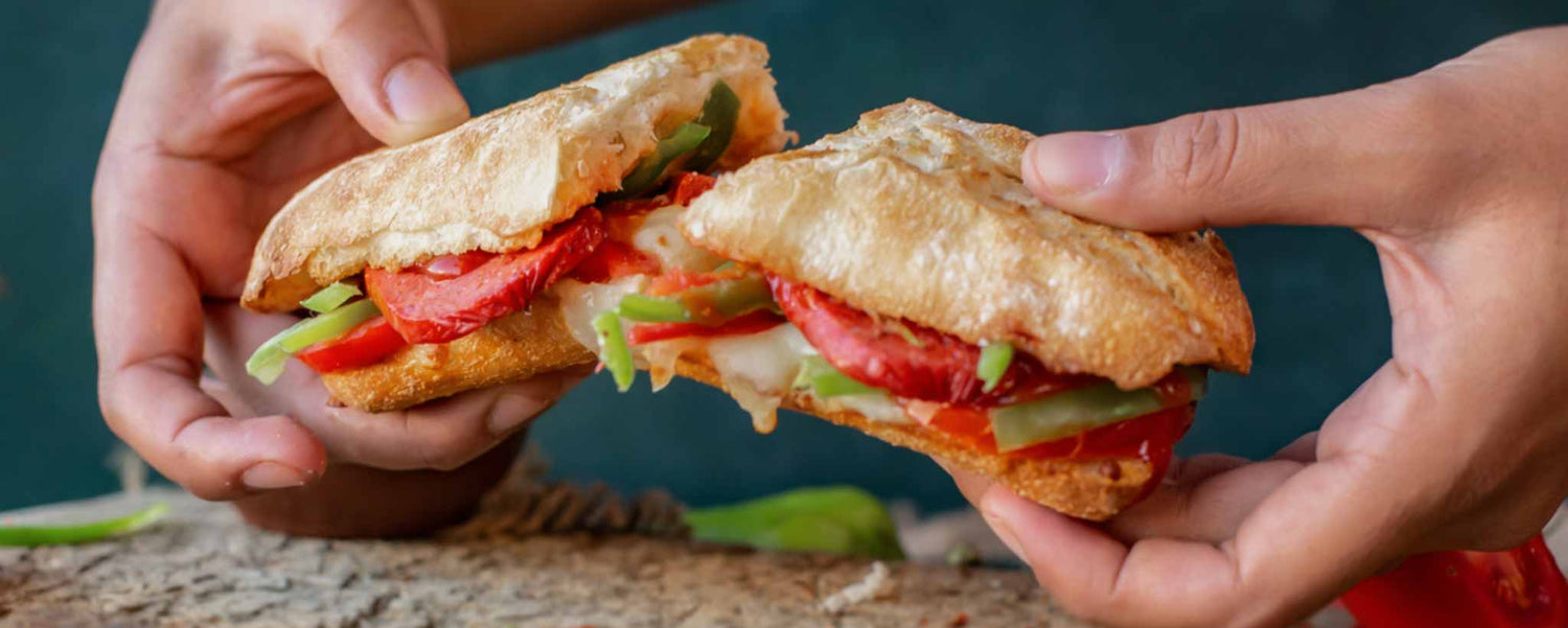 Two hands holding a sandwich cut in half, revealing layers of bread, tomato, lettuce, and cheese.