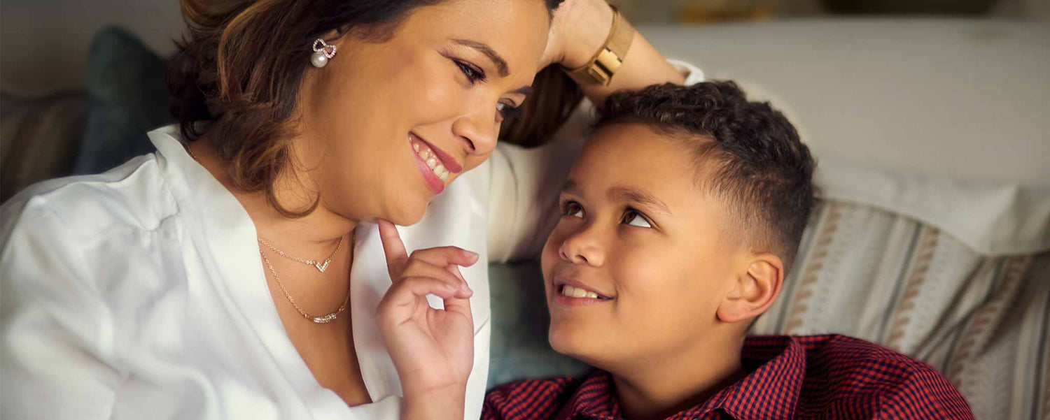 A mother and her young son sit together on a couch, smiling.