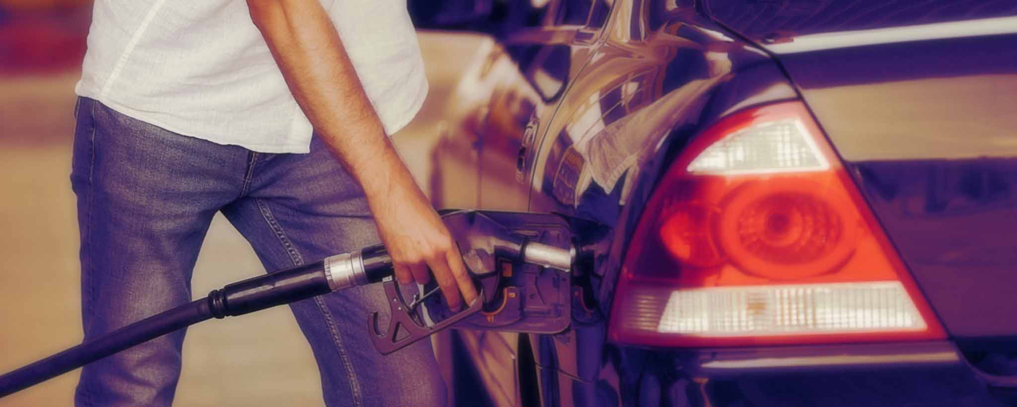 'A man pumps gasoline into a dark car.'