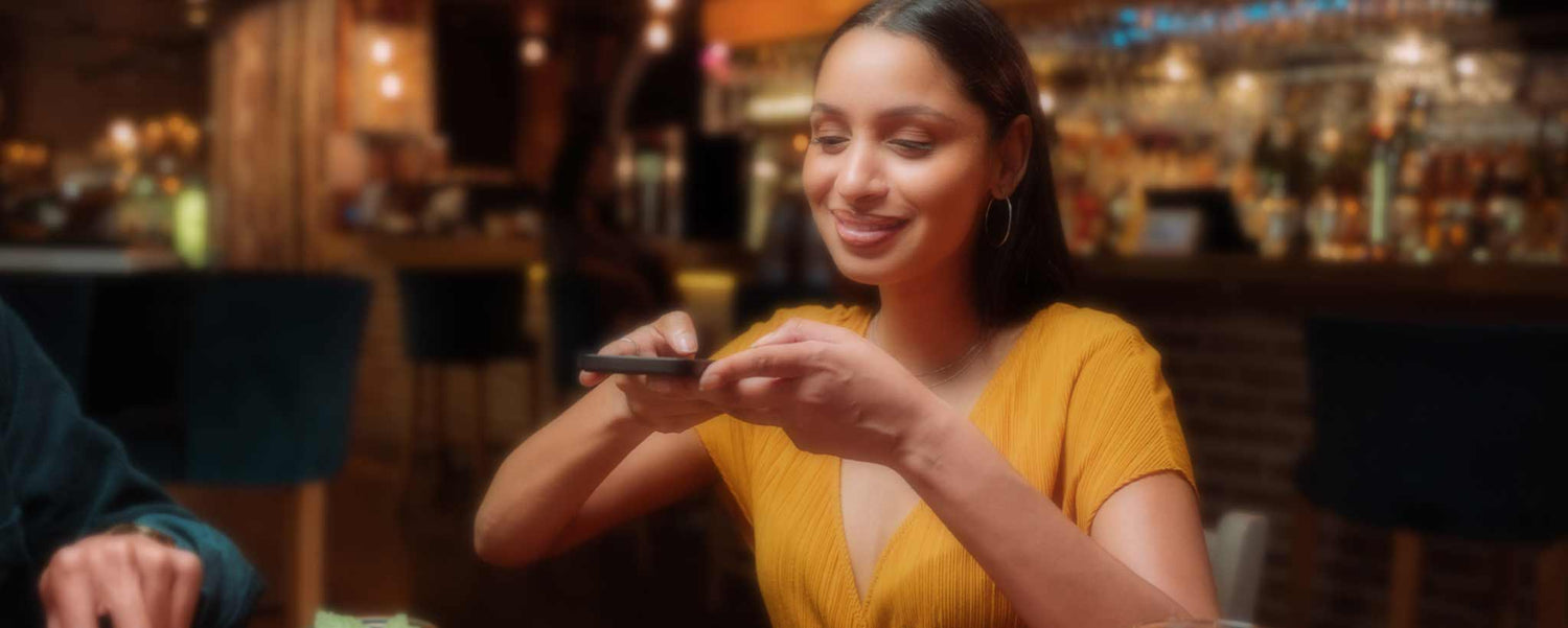 A beautiful young lady photographs her restaurant meal.