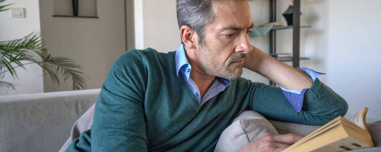 A man reads a paperback book on his sofa.