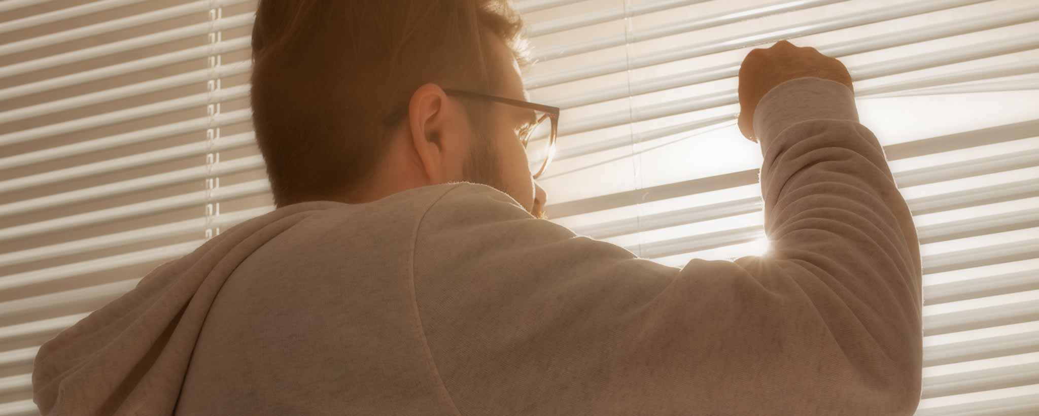 'A man peeks through window blinds.'