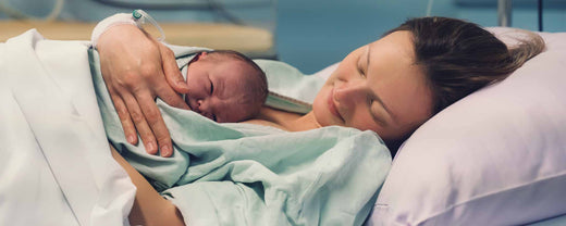 Mother holding a newborn infant while lying in bed at the hospital.