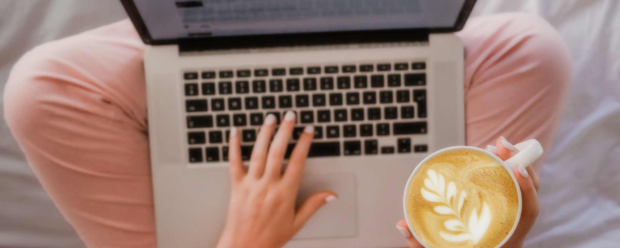 'Woman sits with laptop on her lap and cappuccino in her hand'