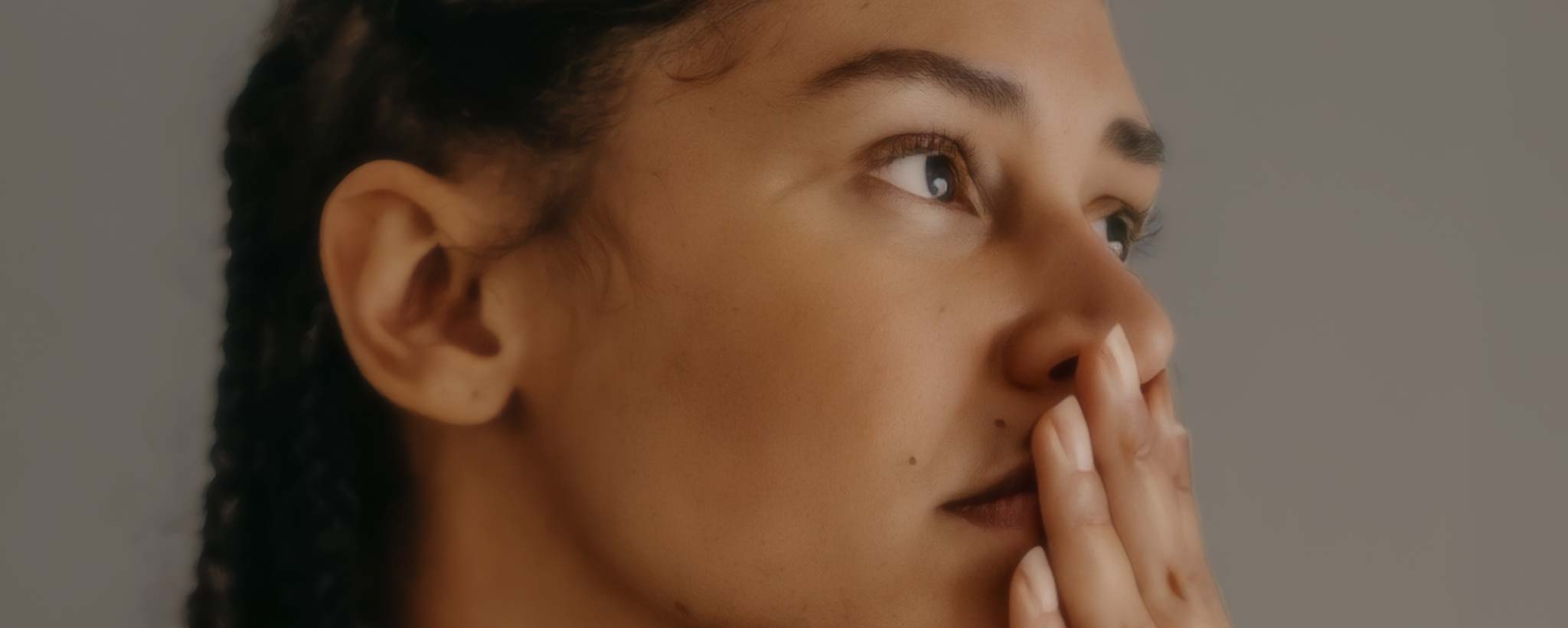 'A pensive Black lady holds her fingers to her lips while looking in the distance.'