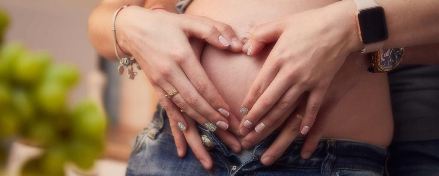 Four hands hold a pregnant belly.