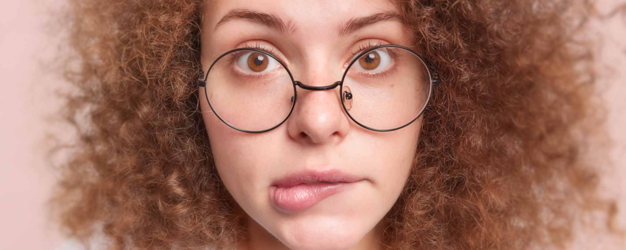 'Close-up of a person with curly red hair and glasses biting her lip.'