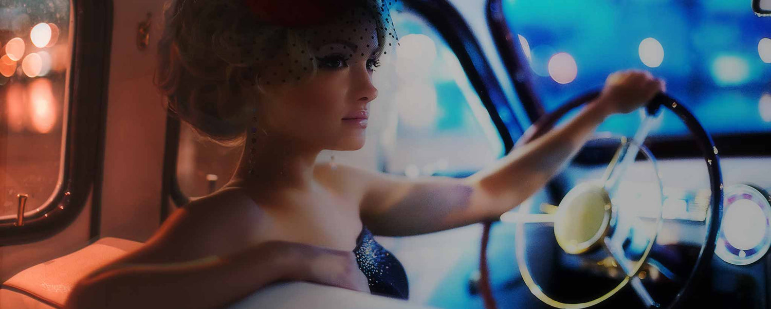 A retro blonde sits the in driver’s seat of classic car.