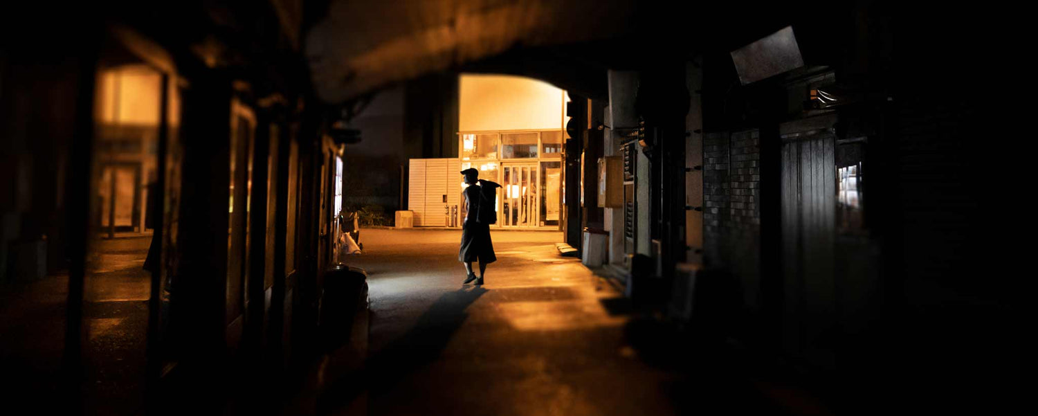 A lone figure walking in shadowing darkness.