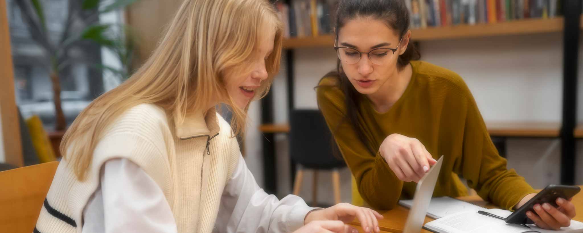 'Two teen female students study in the college library.'