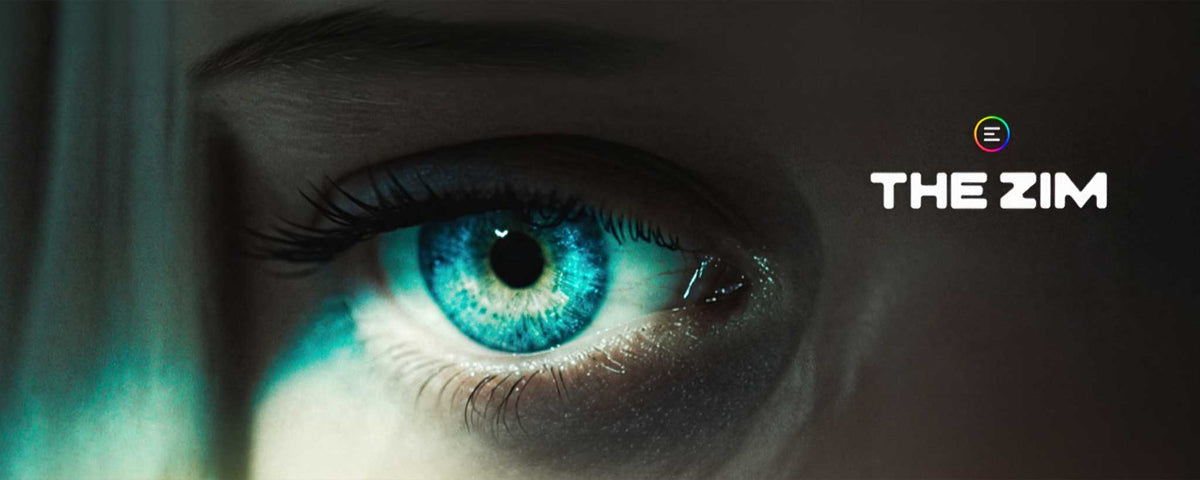 A dramatic close-up of a human eye with vivid blue-green irises, set against a dark shadowed face. The text 'THE ZIM' appears on the right with a small rainbow-colored circular logo above it.