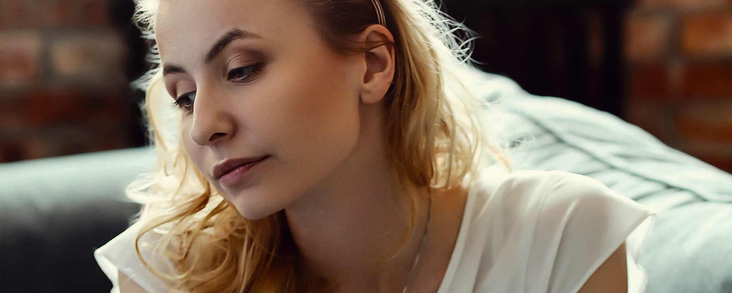 A blonde female worries on a sofa.