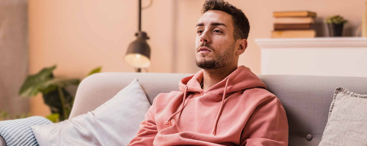 A man in a pink hoodie is sitting on a couch in a living room.