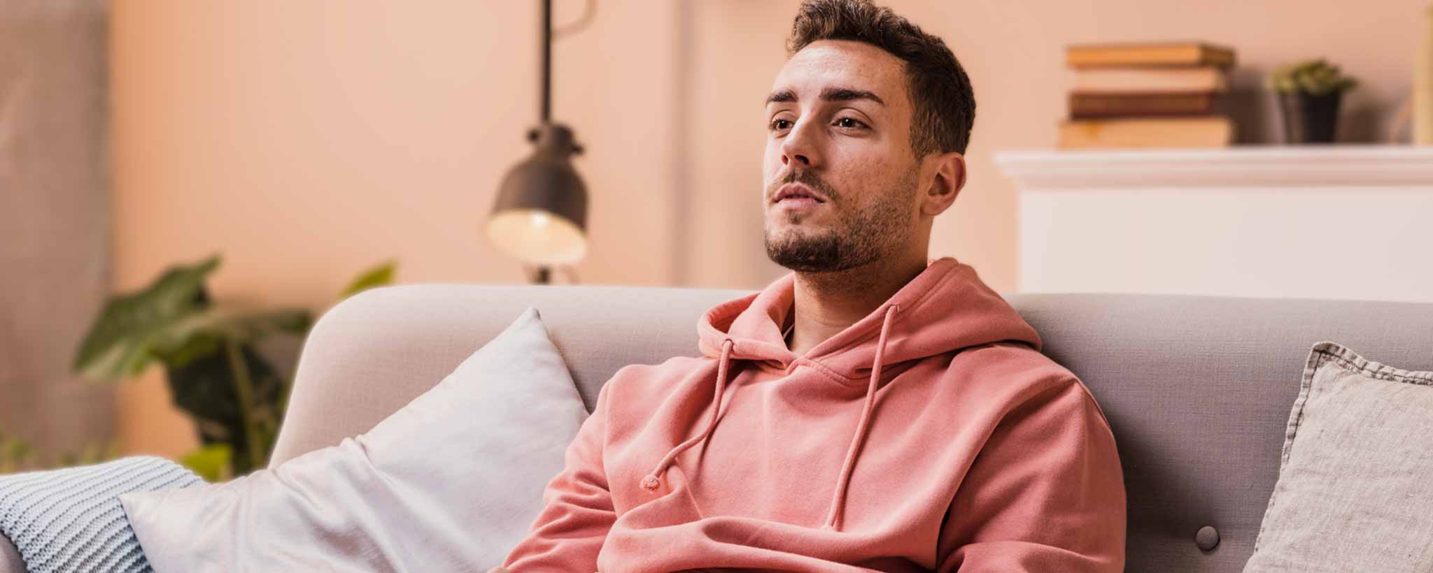 'A man in a pink hoodie is sitting on a couch in a living room.'