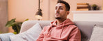 A man in a pink hoodie is sitting on a couch in a living room.