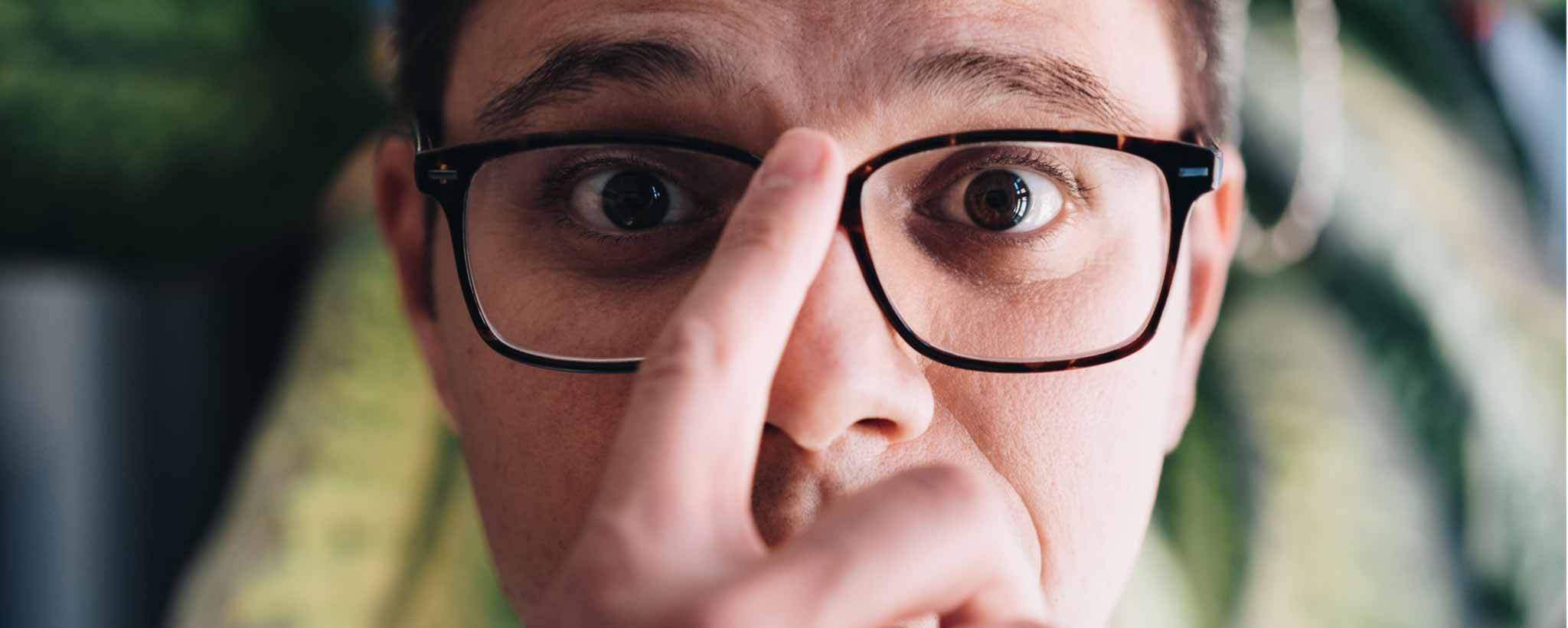 'Person wearing glasses with a hand touching the frame, blurred background.'