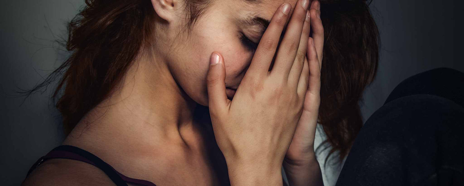 A sad young lady cowering in darkness with her hands over her face.