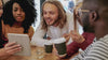 Multi-ethnic young adults watching a tablet in a coffee shop.